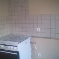 Fragment kuchni z płytkami ceramicznymi w kratkę na ścianie nad kuchenką gazową. Widoczna biała kuchenka, gniazdko elektryczne i fragment blatu.