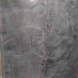 Szara ściana z efektem dekoracyjnym imitującym kamień, widoczne nieregularne wzory i delikatny połysk.