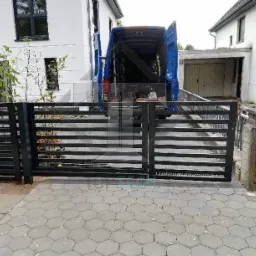 Nowoczesna, pozioma brama wjazdowa z czarnych, metalowych profili, z otwartym busem dostawczym w tle, na tle białego domu z garażem.