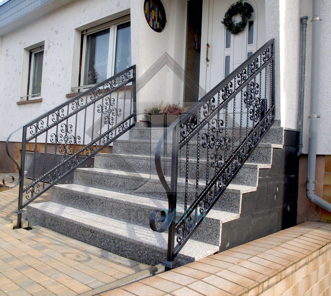 Kute balustrady schodowe z ozdobnymi elementami na zewnątrz domu, widoczne szare granitowe stopnie i białe ściany budynku.