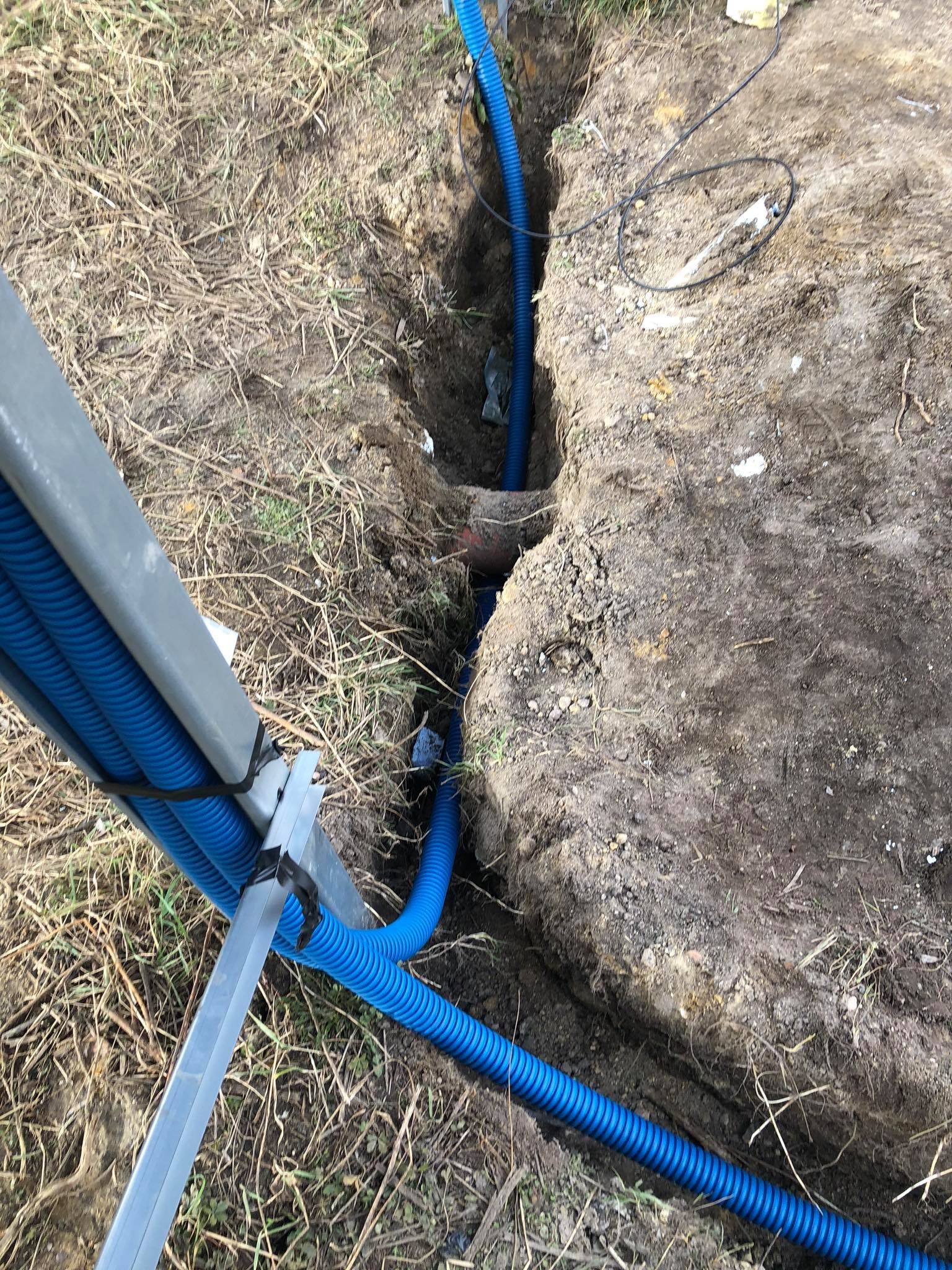 Niebieskie rury karbowane prowadzone w wykopie ziemnym, prawdopodobnie instalacja elektryczna dla paneli słonecznych.
