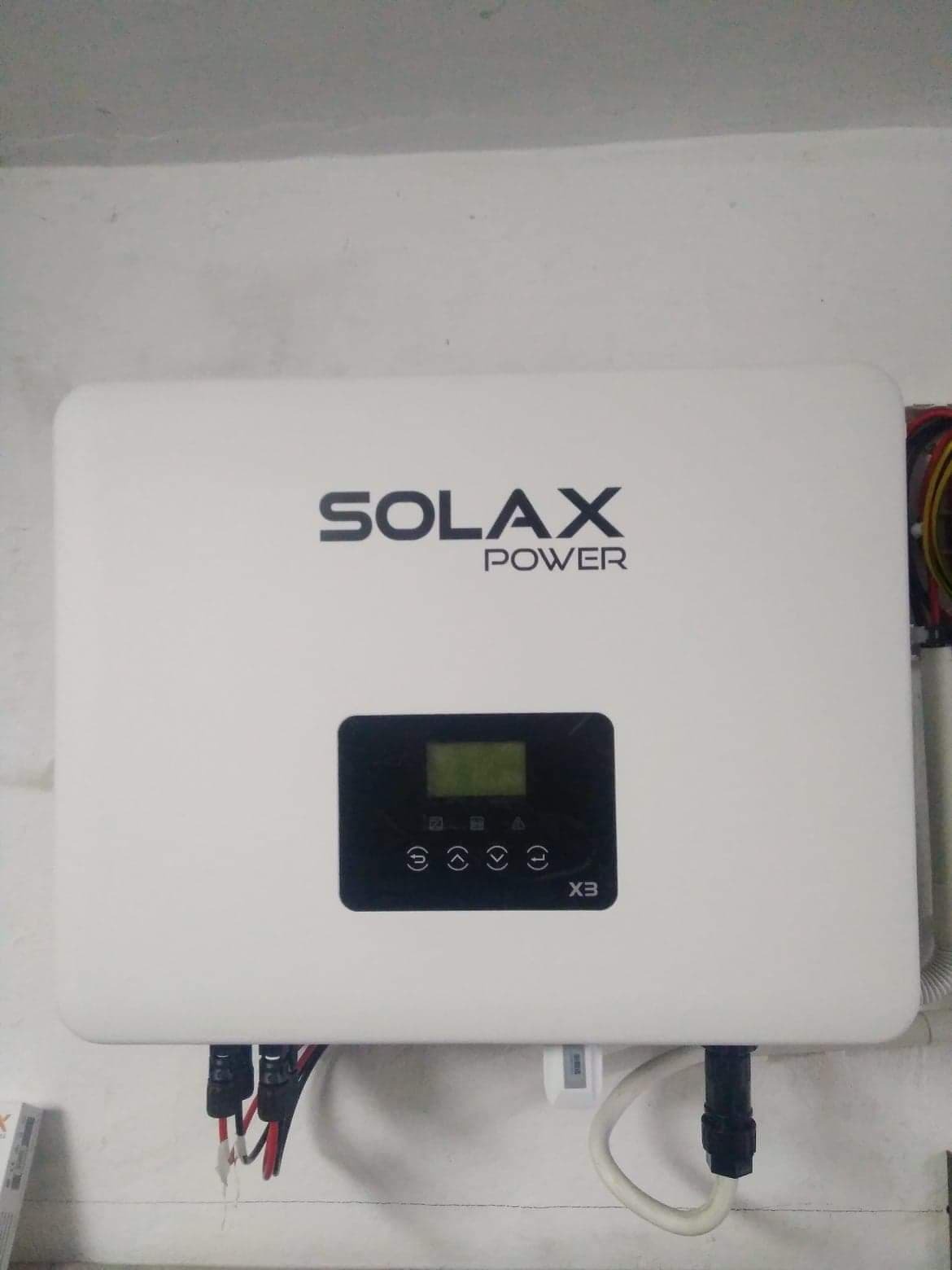 Biały inwerter Solax Power X3 zamontowany na ścianie, widoczne podłączenia przewodów i wyświetlacz.