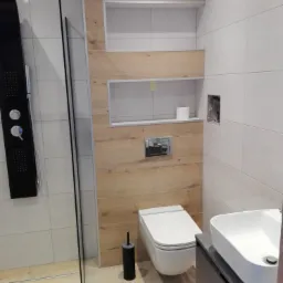 Nowoczesna łazienka z kabiną prysznicową typu walk-in, toaletą wiszącą, umywalką nablatową i drewnopodobnymi panelami na ścianie z wnękami.