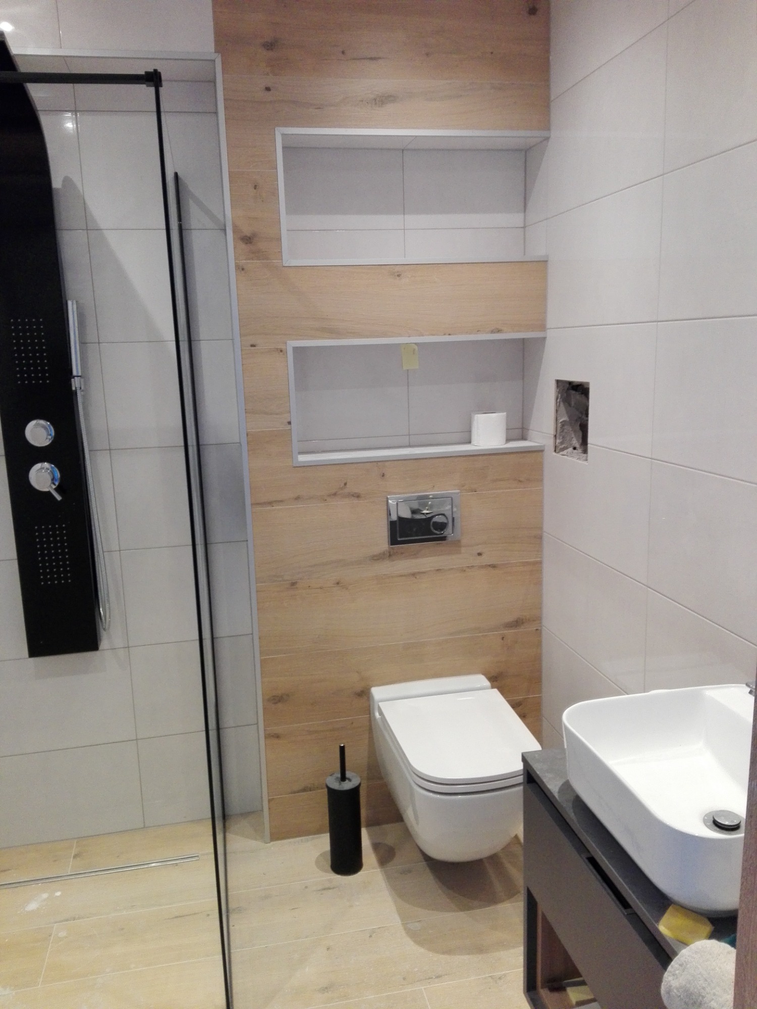 Nowoczesna łazienka z kabiną prysznicową typu walk-in, toaletą wiszącą, umywalką nablatową i drewnopodobnymi panelami na ścianie z wnękami.