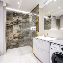 MIKS-MEBLE KRZYSZTOF KORZEŃ - Nowoczesna łazienka z kabiną typu walk-in, marmurowymi płytkami i białymi szafkami z złotymi uchwytami, pralka Samsung widoczna w zabudowie.