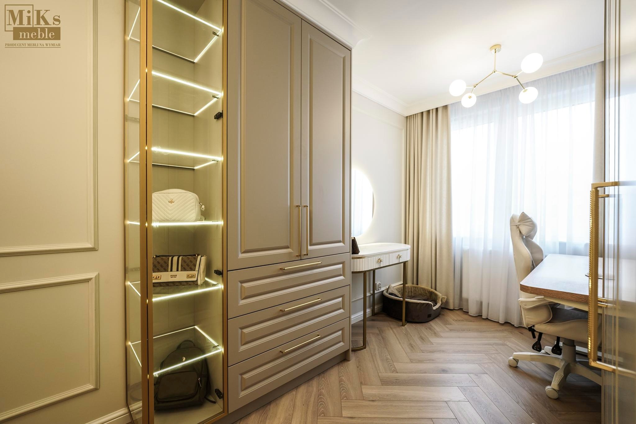 Beżowa garderoba z oświetleniem LED i szklanymi półkami, na których leżą torebki. W tle biurko, krzesło i okno z zasłonami, parkiet w jodełkę.