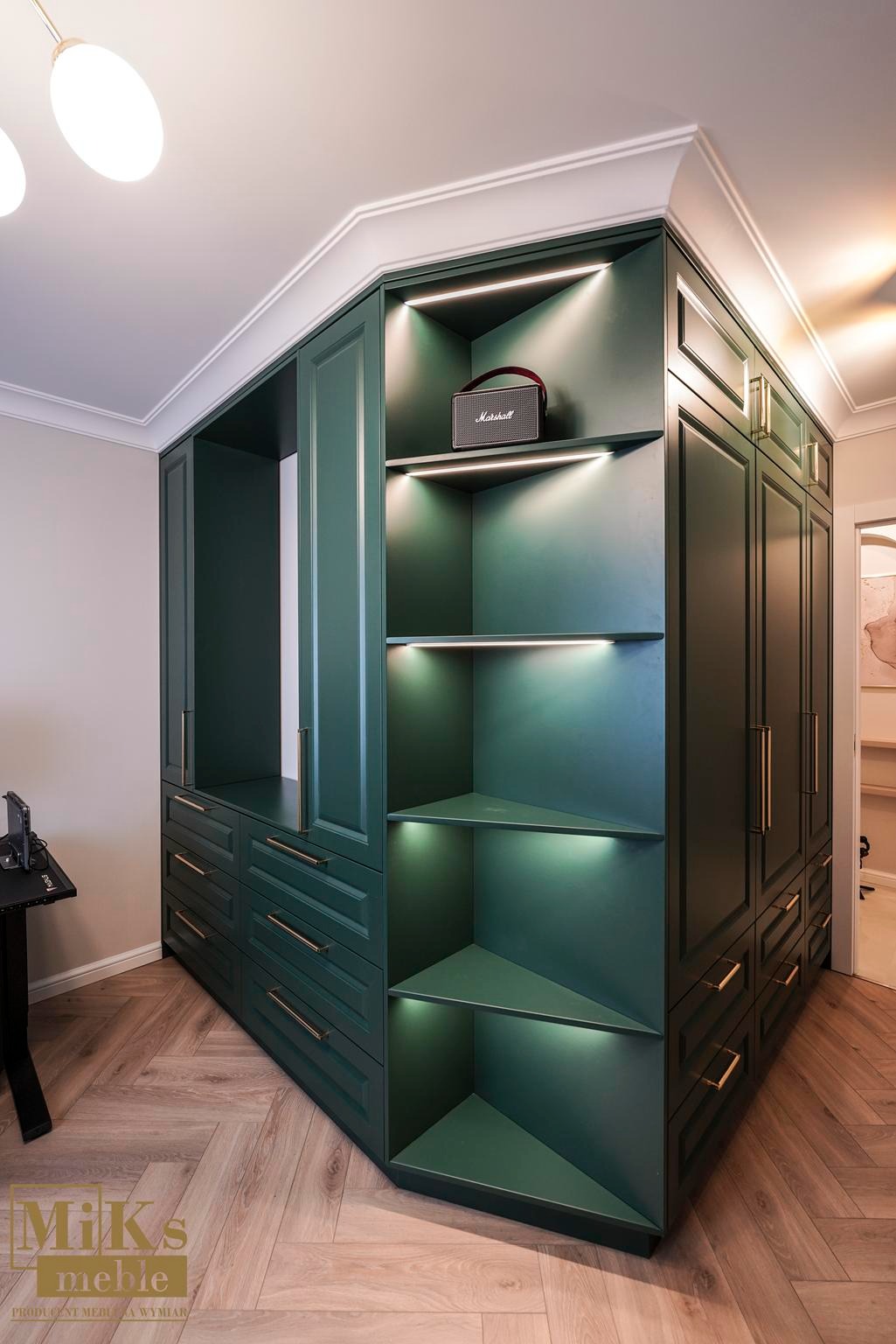 Zielona zabudowa meblowa z szufladami i półkami z podświetleniem LED, uzupełniona o dekoracyjny głośnik Marshall na jednej z półek. Parkiet ułożony w jodełkę.