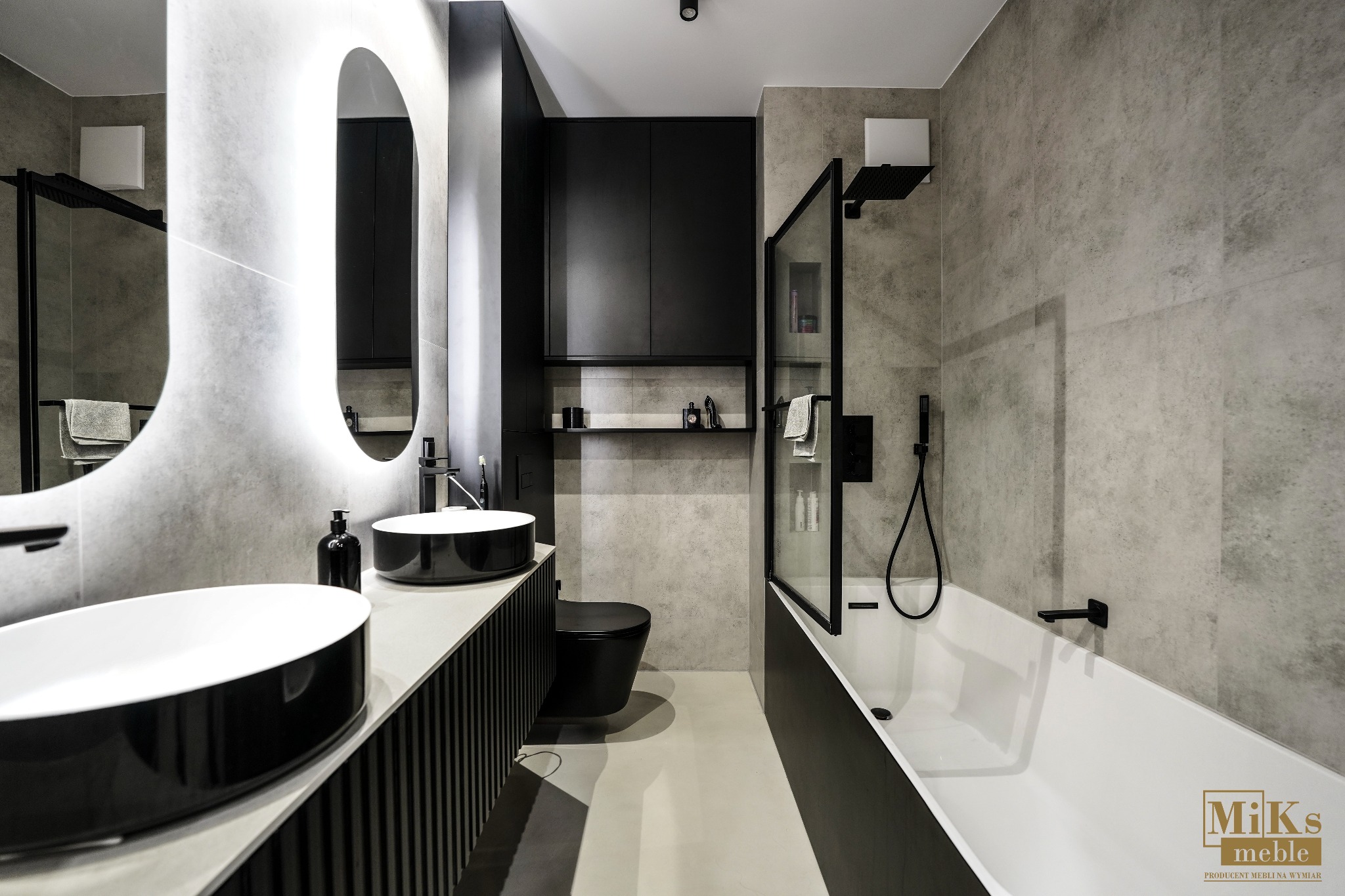 Nowoczesna łazienka w szarościach z czarnymi akcentami: umywalki nablatowe, toaleta i szafki. Owalne lustro z podświetleniem LED. Minimalistyczny design.
