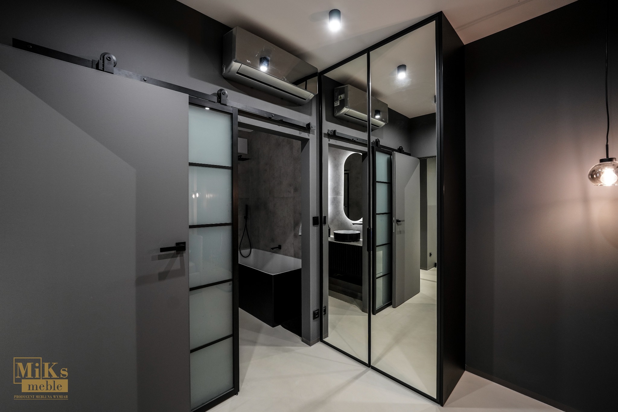 Nowoczesna łazienka w odcieniach szarości z przesuwnymi drzwiami i lustrem, odbijającym wnętrze. Minimalistyczny design podkreśla wisząca lampa i klimatyzacja.