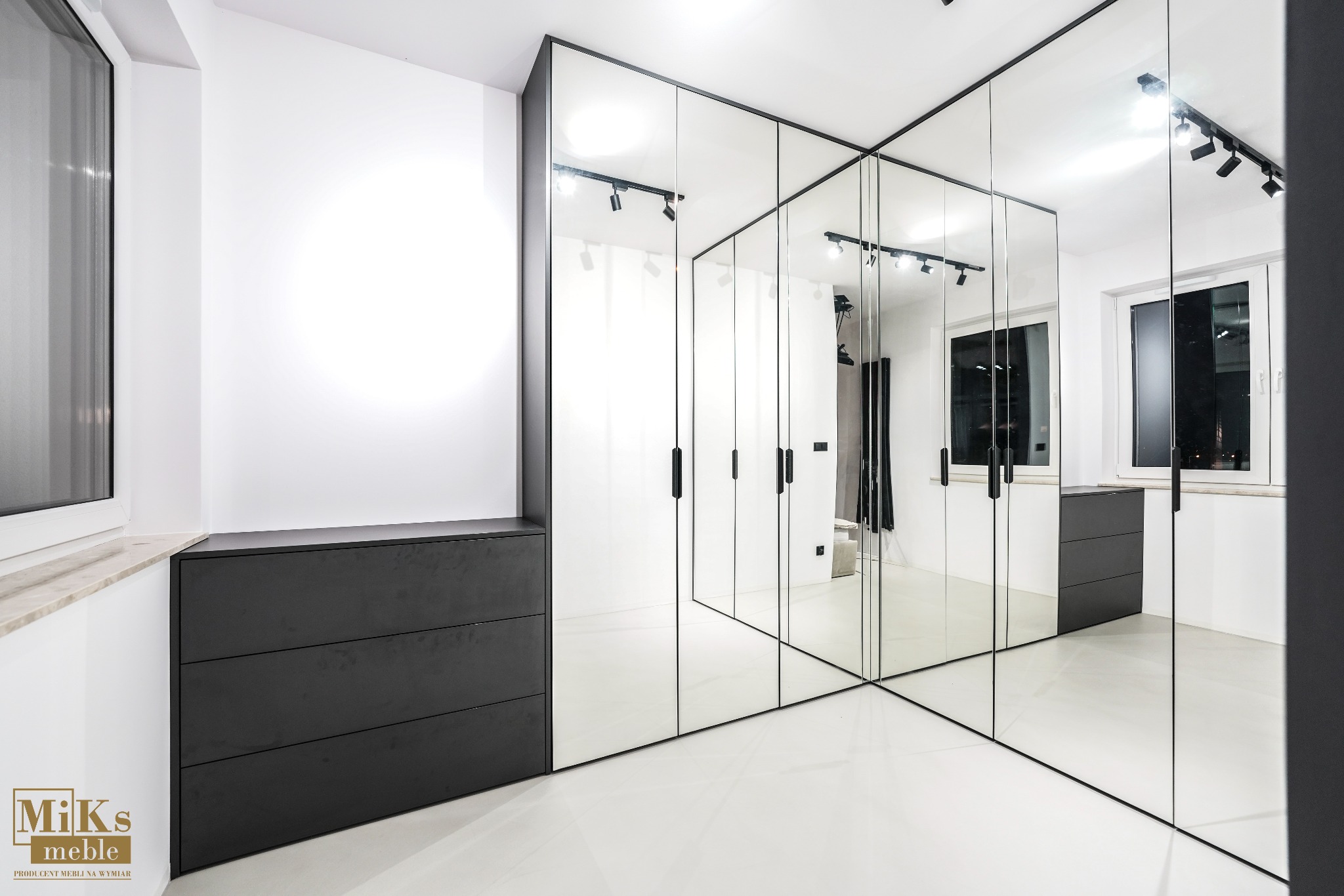 Nowoczesna garderoba z lustrzanymi drzwiami i czarnymi akcentami, oświetlona punktowo, z widoczną komodą. Minimalistyczny design, jasne wnętrze.