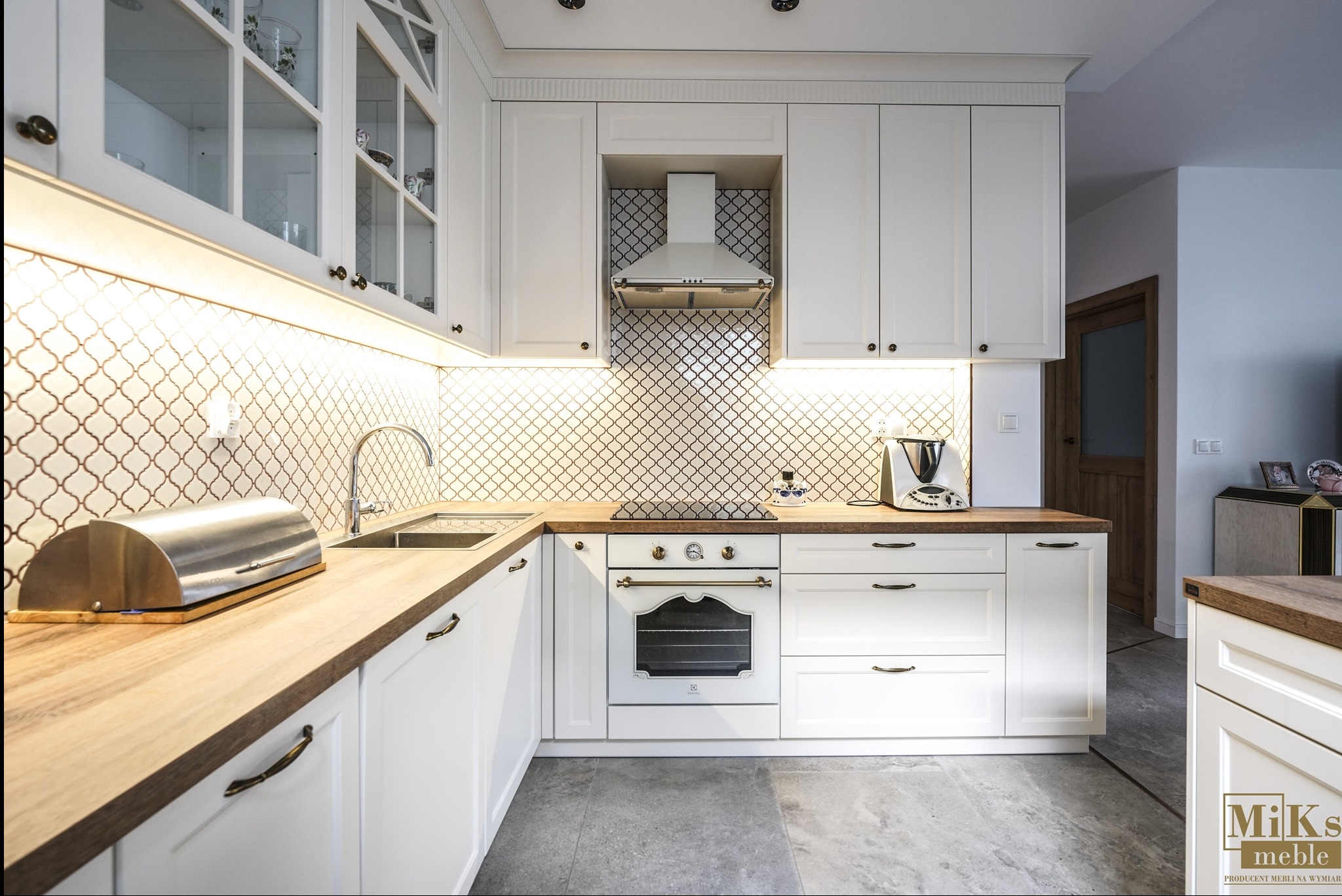 Biała kuchnia z drewnianymi blatami i mozaiką. Uwagę przykuwa piekarnik w stylu retro, dopasowany do reszty zabudowy.