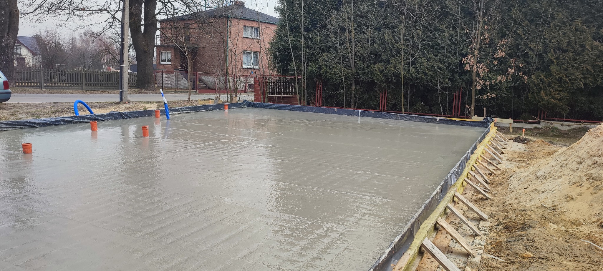 Wylany fundament w Sosnowcu, widoczne pomarańczowe rury i szalunek, w tle zabudowa jednorodzinna.