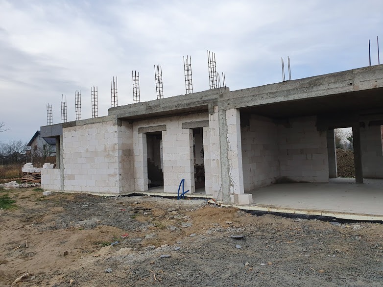 Surowy stan budynku w trakcie wznoszenia ścian z betonu komórkowego Ytong, widoczne wystające pręty zbrojeniowe i niezabezpieczone otwory okienne i drzwiowe.