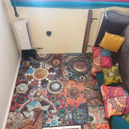 PHU MARTIV Mariusz Żuczkowski - Widok z góry na wnętrze pokoju z zamontowanym klimatyzatorem ściennym AUX, wzorzystą mozaikową podłogą, brązową sofą i dekoracyjnymi poduszkami w odcieniach żółci, zieleni i pomarańczy.