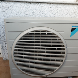 PHU MARTIV Mariusz Żuczkowski - Zewnętrzna jednostka klimatyzacji Daikin zamontowana przy ścianie budynku o nierównej, białej fakturze. Widoczny fragment okna po lewej stronie.