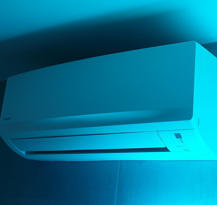 Biała jednostka wewnętrzna klimatyzacji Daikin zamontowana na ścianie, oświetlona niebieskim światłem.