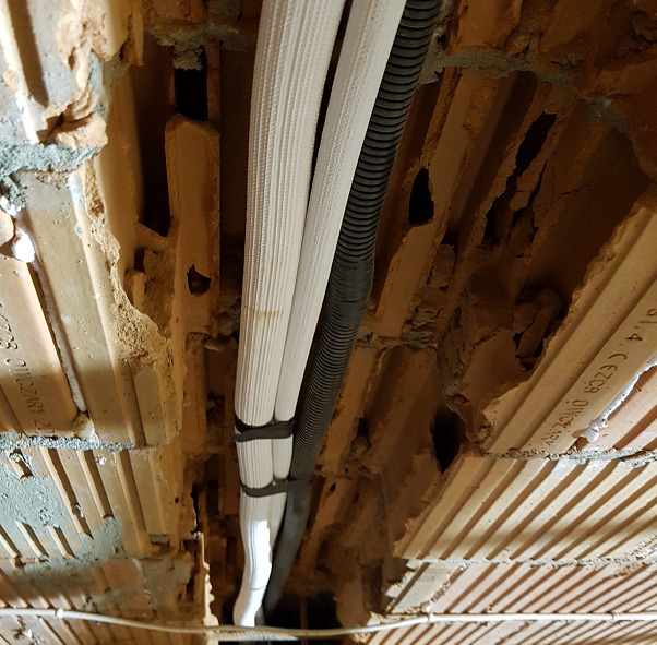 Instalacja klimatyzacji: rury chłodnicze w izolacji oraz rura karbowana prowadzone w wyżłobieniu w ceglanym stropie, widoczne ślady po kuciu.