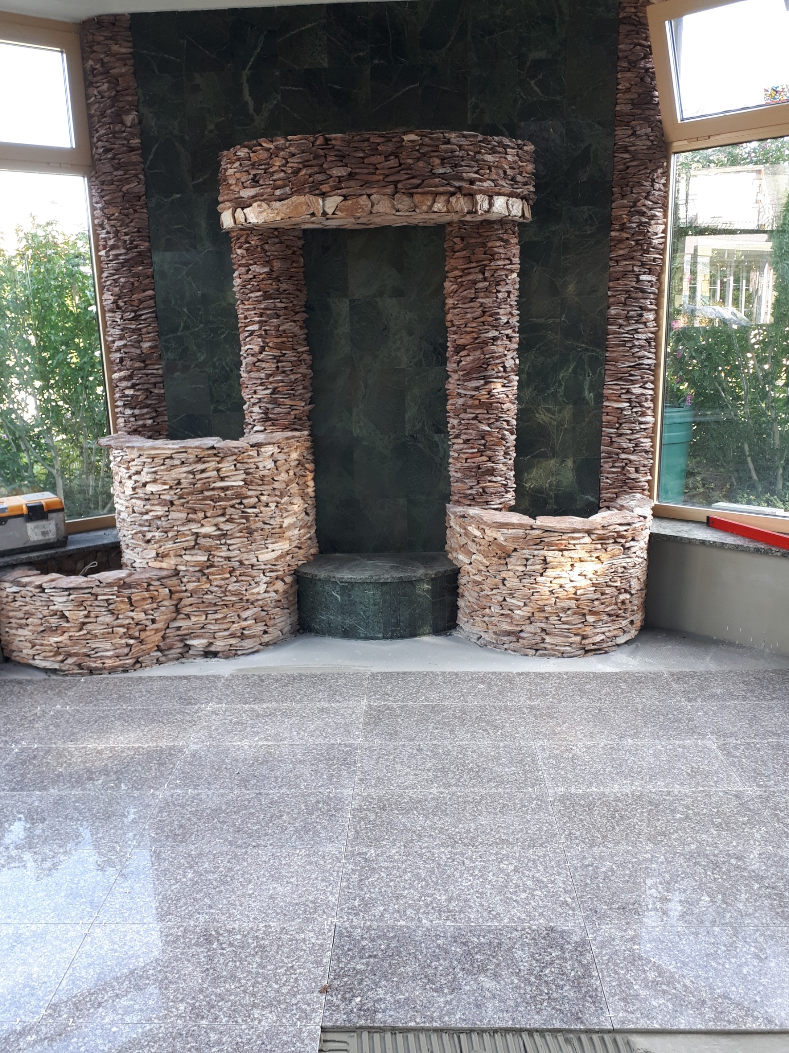 Wykończona wnęka z zielonego marmuru i obłożona kamieniem, z nową podłogą z płytek, widok na okno i skrzynkę narzędziową.