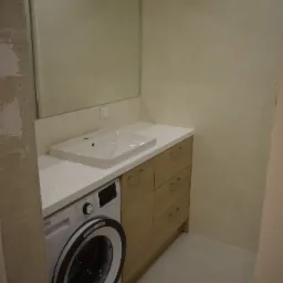 Nowoczesna łazienka z umywalką nablatową, szafką z drewnianymi frontami i pralką pod blatem, widok z niedokończonego remontu.