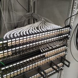 Inneco - Panel krosowniczy z podłączonymi kablami sieciowymi w szafie rack, widoczne numery portów i uporządkowane wiązki kabli.