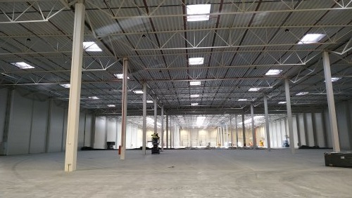 Przestronne wnętrze hali magazynowej z widoczną konstrukcją stalową dachu, słupami nośnymi i oknami dachowymi, przygotowane do instalacji systemów elektrycznych.