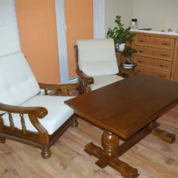 Dwa drewniane fotele z białymi poduszkami obok ciemnobrązowego stołu na tle komody i pomarańczowych rolet w pokoju dziennym.