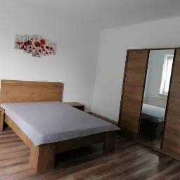 Komplet mebli do sypialni z łóżkiem z drewnianą ramą, szafkami nocnymi i dużą szafą z lustrzanymi drzwiami, na ścianie dekoracja z motywem czerwonych maków.