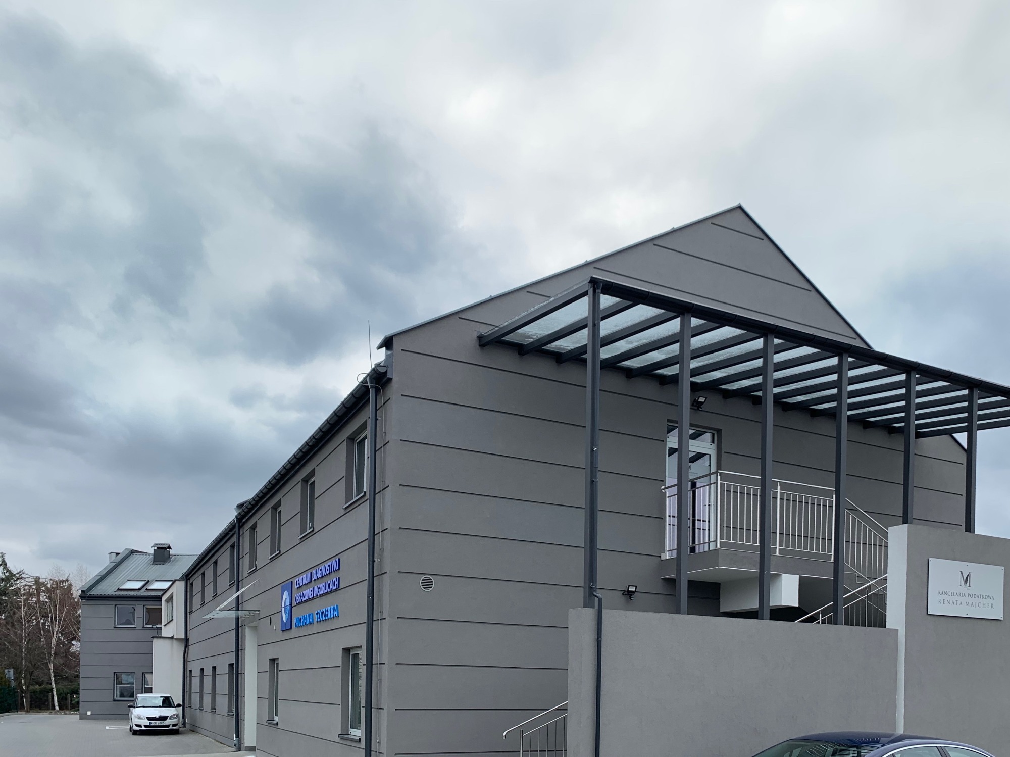 Elewacja budynku biura rachunkowego z szyldem 'Kancelaria Podatkowa Renata Majcher' oraz napisem 'Centrum Diagnostyki Obrazowej w Gorlicach', widok z zewnątrz w pochmurny dzień.