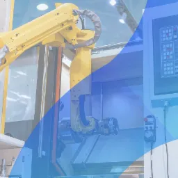 Żółty robot przemysłowy z manipulatorem, sterowany za pomocą panelu kontrolnego z ekranem i przyciskami, w hali produkcyjnej.