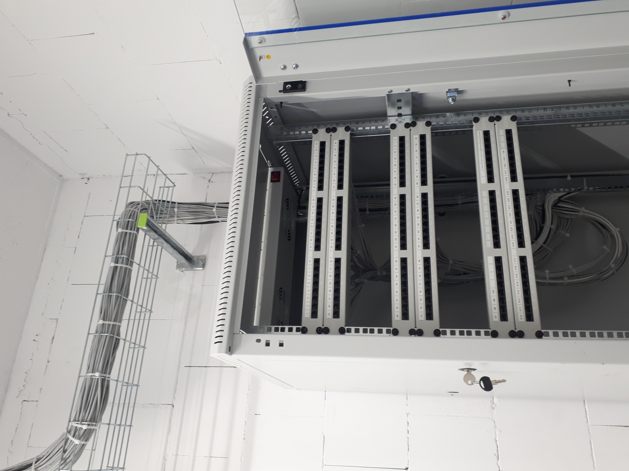 Szafa serwerowa z panelami krosowniczymi i okablowaniem w korytku, zamontowana w pomieszczeniu w Pruszkowie. Widoczny klucz w zamku szafy.