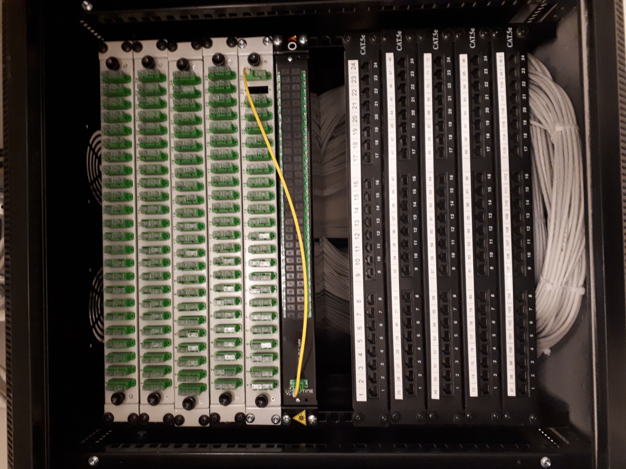Panel krosowniczy z podłączonym kablem światłowodowym w szafie rack, widoczne porty RJ45 i wentylatory chłodzące.