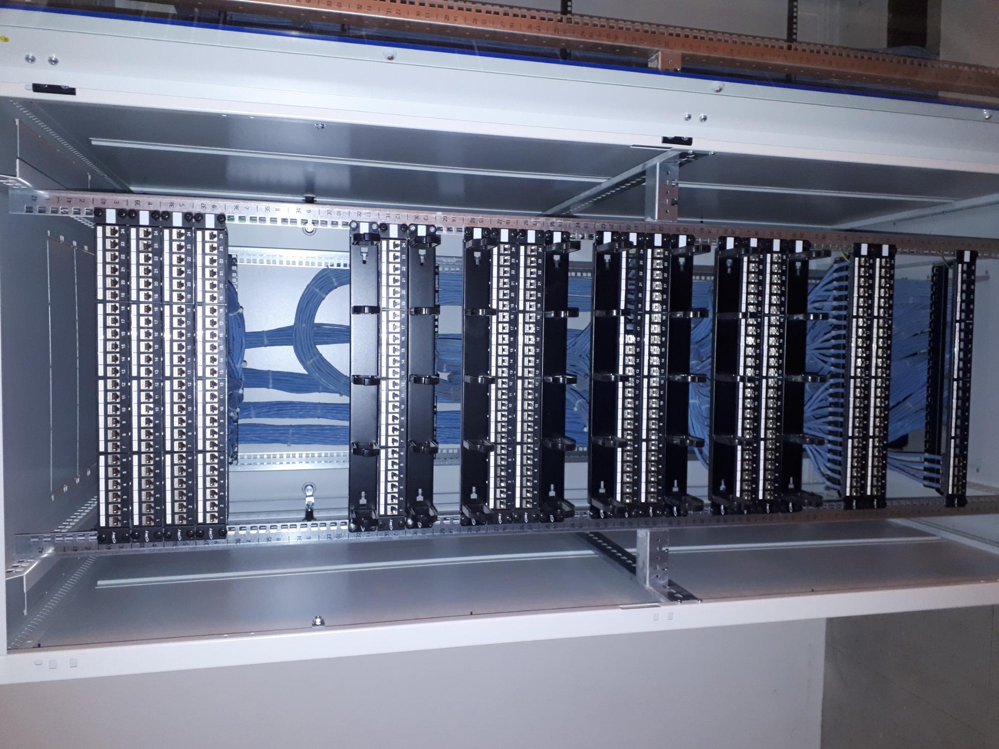 Panel krosowniczy z uporządkowanymi niebieskimi kablami w szafie rack, widok z góry ukazujący precyzję połączeń.