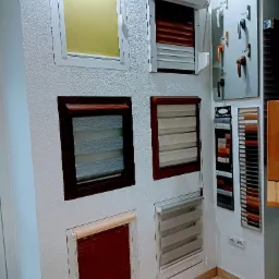 Ekspozycja różnych typów osłon okiennych: rolety zwijane w białej ramie, żaluzje poziome w ramie drewnopodobnej, roleta zewnętrzna z listwami w kolorze drewna, paleta kolorów i wzornik klamek...