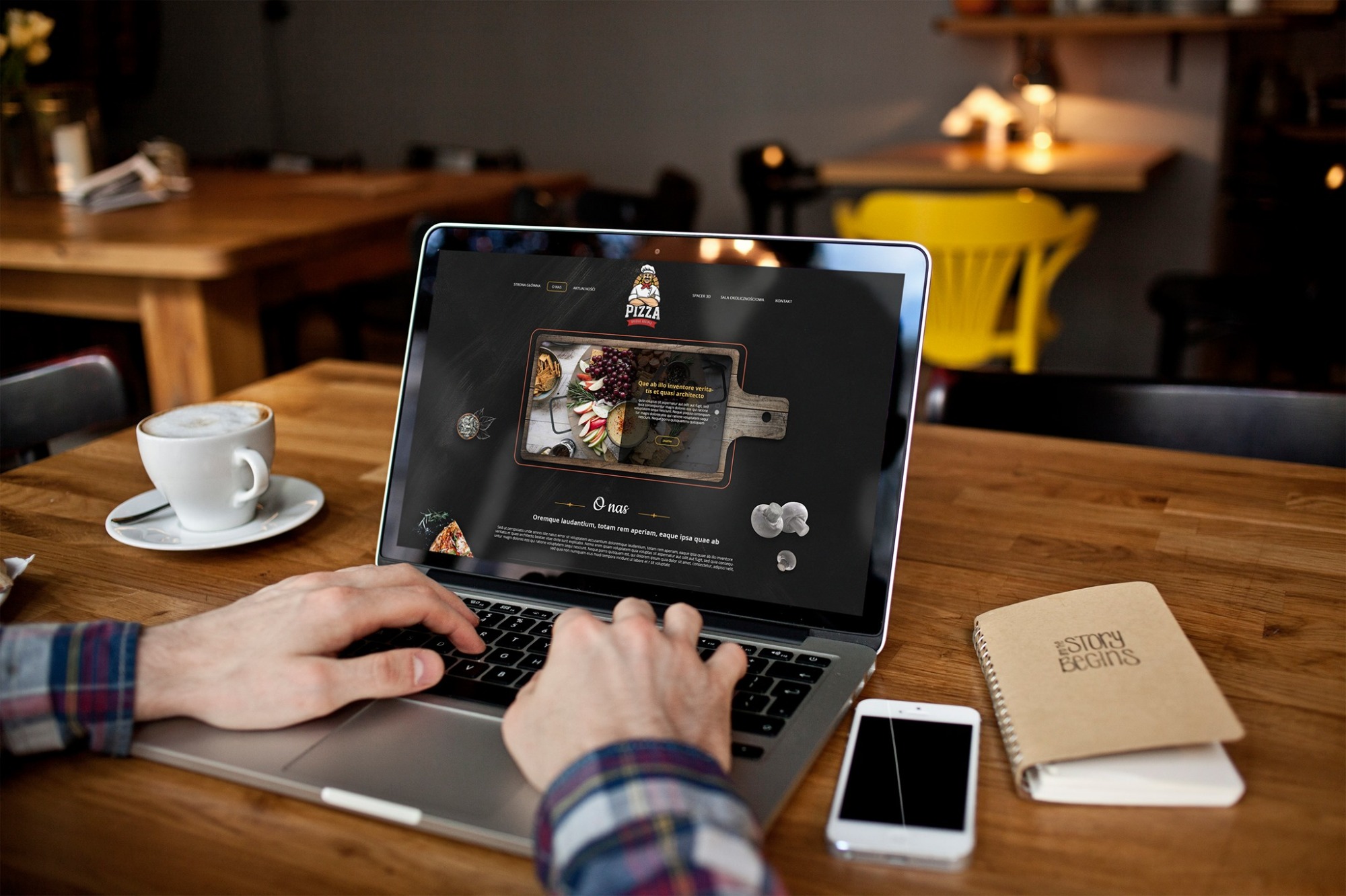 Osoba pisze na laptopie prezentującym projekt strony internetowej pizzerii, z kawą i notatnikiem na drewnianym stole w kawiarni.
