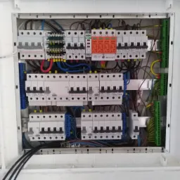 Rozdzielnica elektryczna z zainstalowanymi bezpiecznikami i przewodami, widok z góry na otwartą skrzynkę, kable w różnych kolorach starannie ułożone.