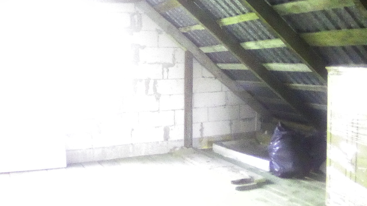 Poddasze w trakcie adaptacji: surowe ściany z bloczków, drewniana konstrukcja dachu, czarny worek na odpady budowlane i fragment płyty izolacyjnej.