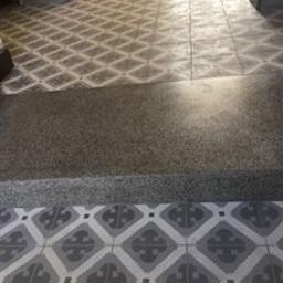 Polfloormax - Fragment posadzki z przejściem od wzorzystych płytek do gładkiej, szarej powierzchni, prawdopodobnie w trakcie renowacji lub łączenia różnych typów wykończenia.