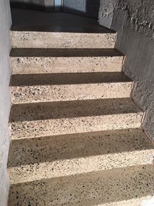 Betonowe schody z widocznym kruszywem, prowadzące w dół, oświetlone naturalnym światłem w surowym wnętrzu.