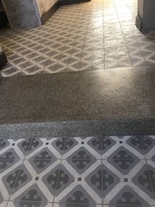 Fragment posadzki z przejściem od wzorzystych płytek do gładkiej, szarej powierzchni, prawdopodobnie w trakcie renowacji lub łączenia różnych typów wykończenia.