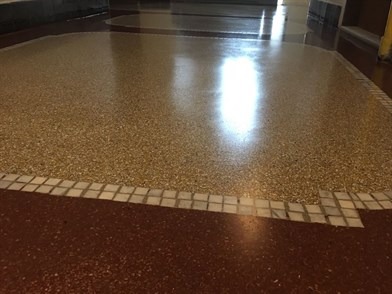 Błyszcząca posadzka przemysłowa z lastryko w odcieniach beżu, oddzielona od czerwonej części podłogi białymi kwadratowymi płytkami.