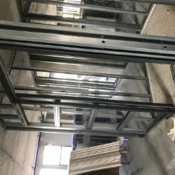 Metalowa konstrukcja sufitu podwieszanego w trakcie montażu, widoczne płyty gotowe do instalacji, surowy betonowy strop w tle.