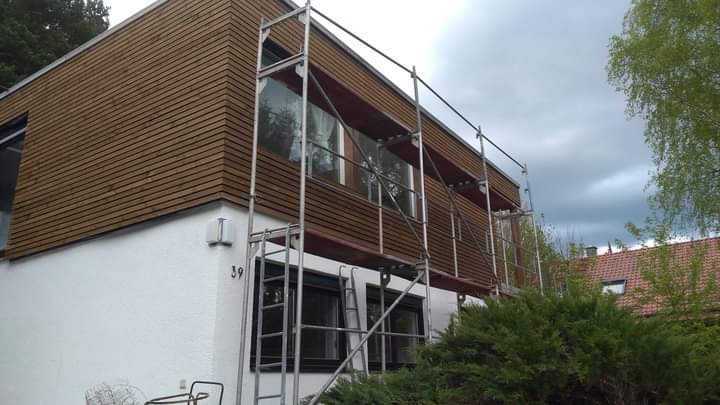 Dom z elewacją z drewnianych paneli, częściowo zasłonięty rusztowaniem. Widoczny numer domu '39'.