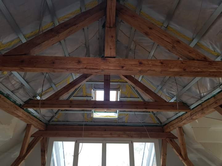 Poddasze z widoczną konstrukcją drewnianą, ociepleniem z folii i wełny mineralnej, okno dachowe w centralnej części dachu, widok od dołu.