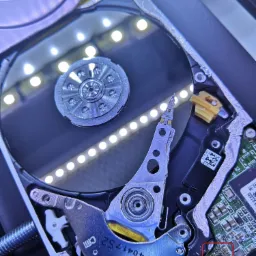 Otwarty dysk twardy z widocznymi talerzami i głowicami, podświetlony listwą LED, z widoczną elektroniką i elementami mechanicznymi.