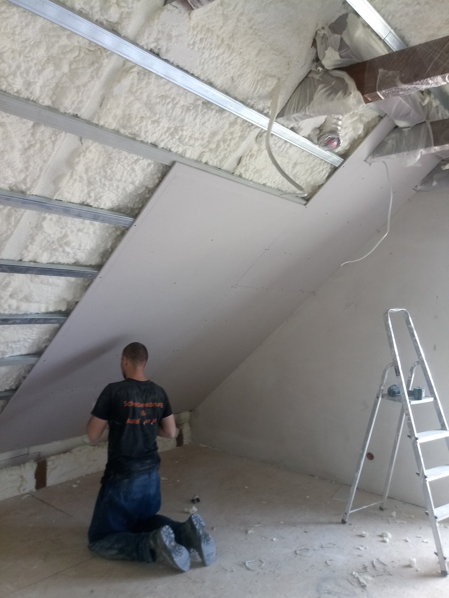 Montaż płyty gipsowo-kartonowej na poddaszu ocieplonym pianką PUR, widoczna drabina i metalowa konstrukcja sufitu