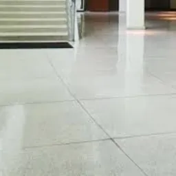 Błyszcząca, jasna posadzka z płytek w przestronnym holu, widoczne schody z metalową balustradą i czarną wycieraczką, minimalistyczny design.