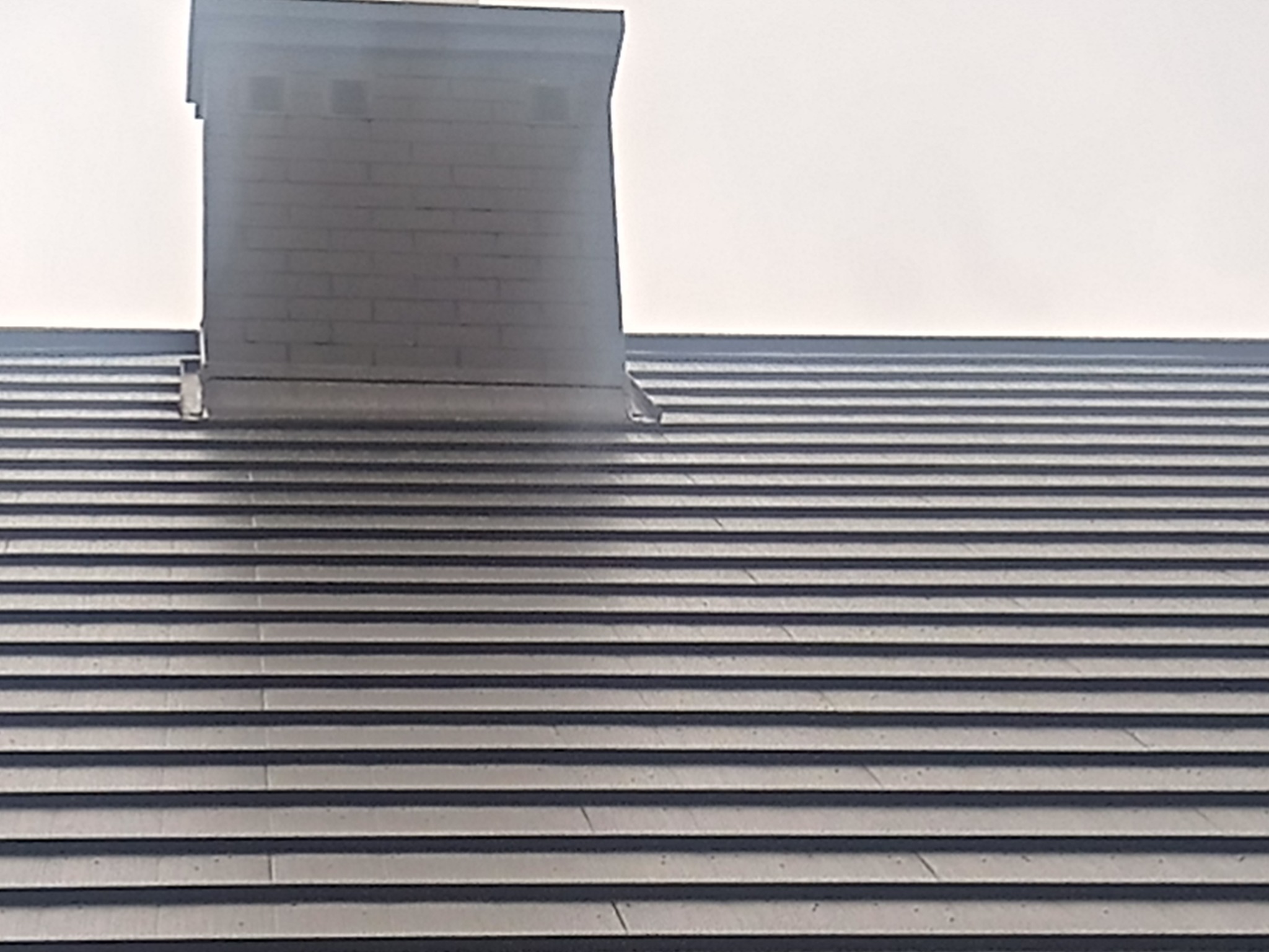 Fragment dachu z kominem w Rzeszowie, widok z bliska na ciemnoszarą dachówkę ułożoną rzędami.