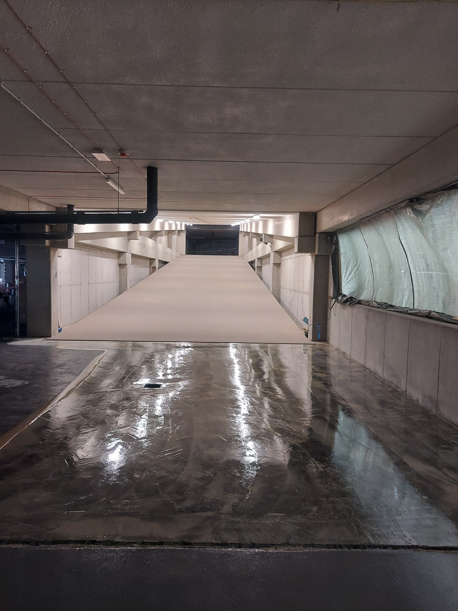 Błyszcząca posadzka w przemysłowym wnętrzu, widoczne odbicia światła, betonowe ściany i sufit z instalacjami.