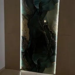 Podświetlona ściana z płytek imitujących marmur w odcieniach zieleni i złota, sąsiadująca z beżowymi płytkami ściennymi i podłogowymi, tworząca dekoracyjny panel w korytarzu.