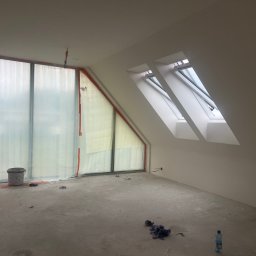 DEVELOPMENT SP Z O O - Poddasze w trakcie prac wykończeniowych: okna dachowe, zabezpieczone folią okno, surowa podłoga. Widoczne ślady po pracach budowlanych, butelka wody.